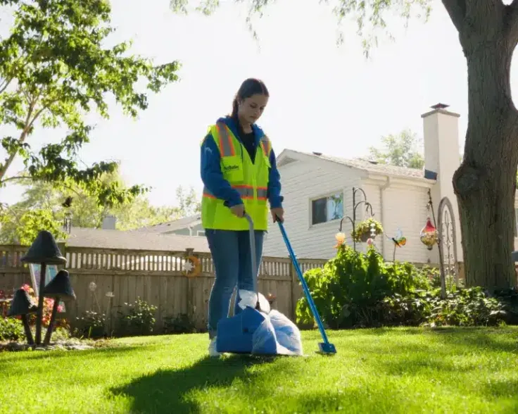 Pet waste being picked up with a scooper by Pet Butler team member with yellow safety vest