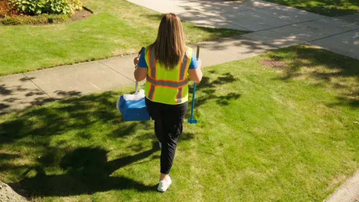 Woman with yellow safety jacket and poop scooper cleaning up dog waste