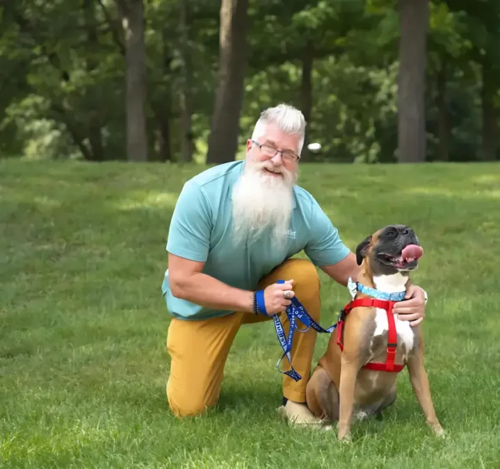 Bryan Peirce, Manager of Pet Butler Columbus OH sitting with a boxer dog breed on a green lawn on a sunny day.