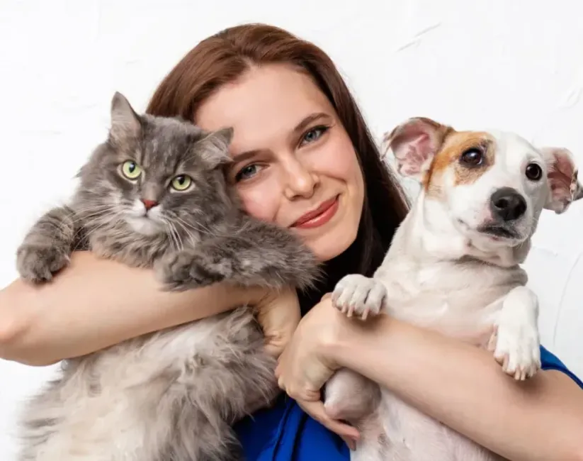 Female Pet Butler pet care professional hugging a grey cat and small white dog to her face.
