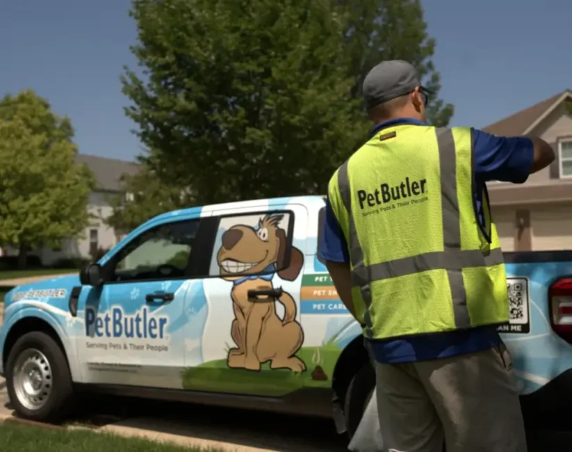 Pet Butler professional in a yellow logoed vest removing an item from the back of a Pet Butler pick up truck.