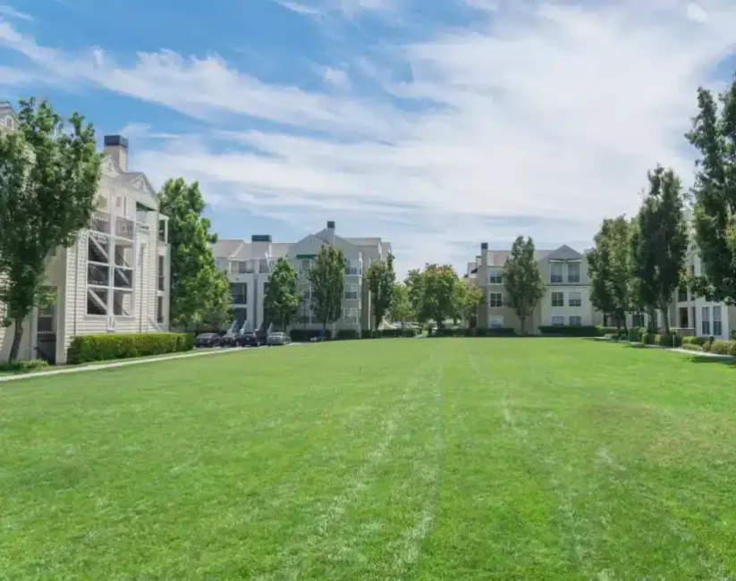 Beige, low-rise, multi-family buildings next to large open grassy area.