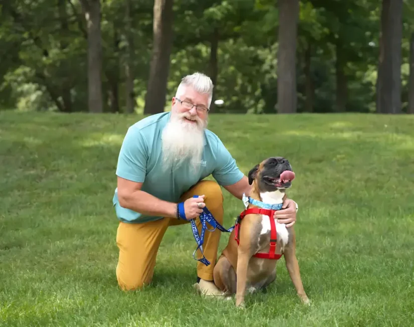 Bryan Peirce, Manager of Pet Butler Columbus OH sitting with a boxer dog breed on a green lawn on a sunny day. Dog Walking - Pet Sitting - Pet Sitter - Pet Care Services - Dog Walker